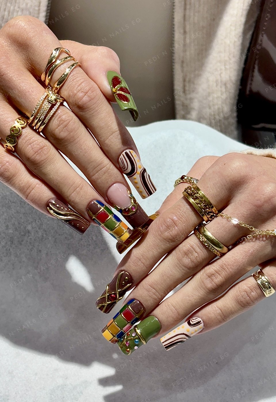 Autumn-toned long square nails with gold-outlined checkerboard, swirl and jewel nail art